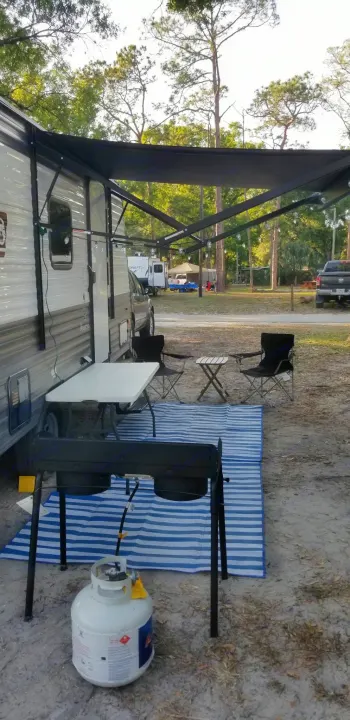 Relaxing RV rental campsite: extended awning over an outdoor cooking setup, table, chairs, and striped mat.. Coleman Lantern 17B 2023