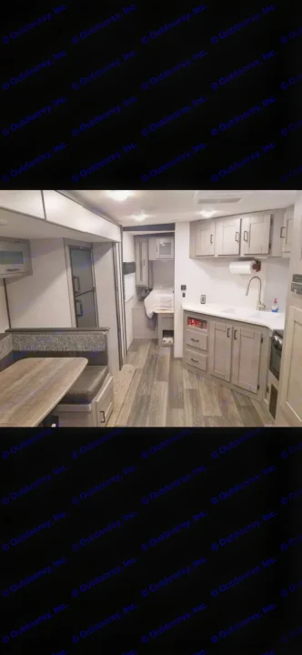 Interior of a modern RV rental, featuring a light gray kitchen with sink, a dark upholstered dinette, and a glimpse of the bedroom area.. Heartland RVs Mallard 2021
