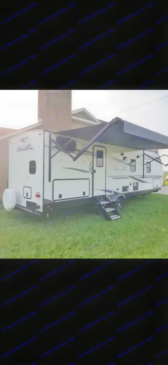 White Mallard travel trailer RV rental, with awning extended and steps, parked on grass beside a house.. Heartland RVs Mallard 2021