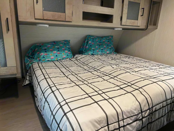 Cozy RV rental bedroom with patterned pillows, plaid comforter, and overhead storage.. Heartland RVs Mallard 2021