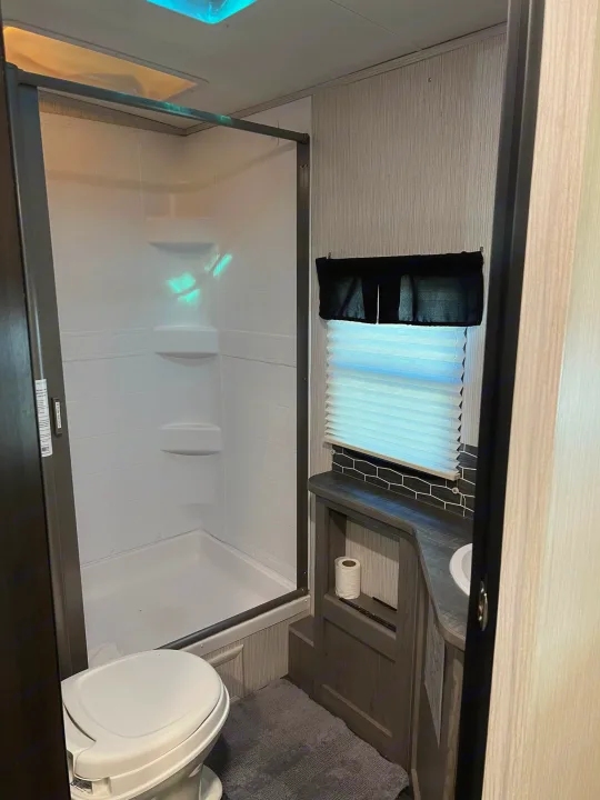 Explore the compact bathroom of this RV rental, featuring a shower, toilet, sink, and window with blinds.. Heartland RVs Mallard 2021