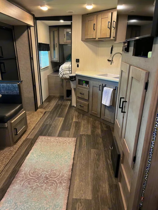 Inside a modern RV rental: a compact kitchen with a sink, adjacent dining, and a cozy bedroom beyond. Perfect for road trips.. Heartland RVs Mallard 2021