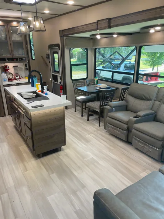 Explore this modern RV rental: a spacious interior featuring a kitchen island, dining area, and comfy recliners.. Grand Design Solitude S-Class 2021