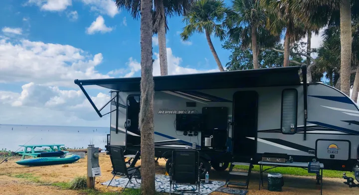Scenic rv rental parked by the water, complete with an outdoor living area, kayak, and fishing gear for a relaxing camp.. Forest River Cherokee Alpha Wolf 2022
