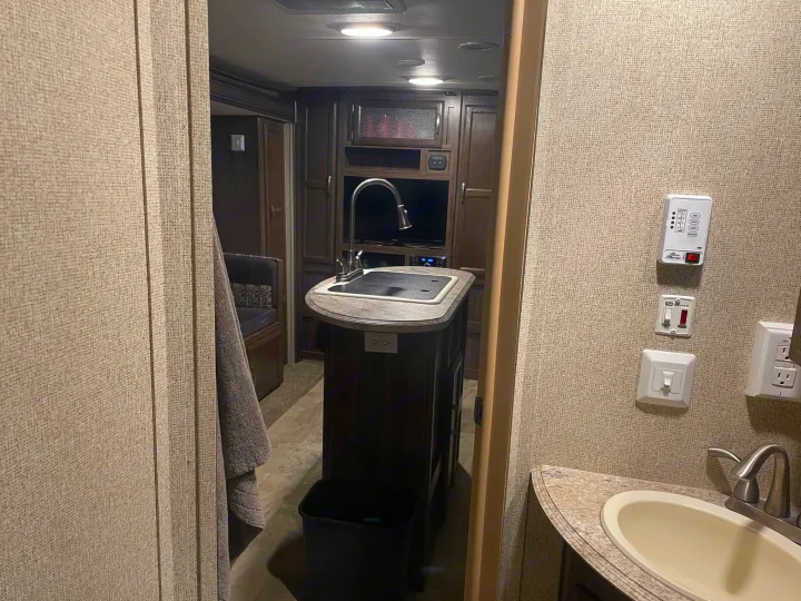 RV rental interior shows a compact kitchen with sink, beyond to the living area, and a partial bathroom view.. Coachmen Apex 2017