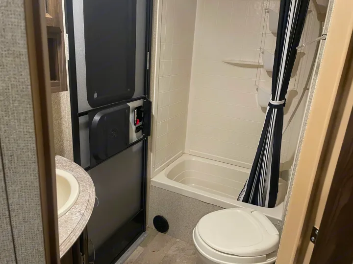 Compact RV rental bathroom with sink, toilet, tub/shower, and striped curtain. An ideal setup for road trips.. Coachmen Apex 2017