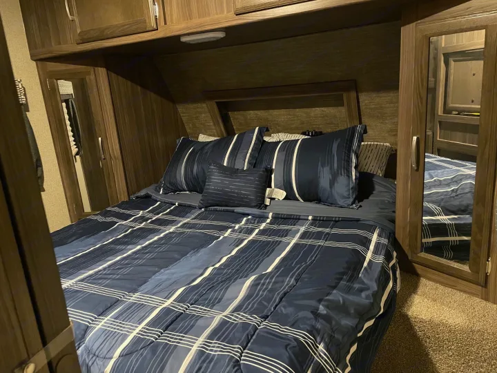 Cozy RV rental bedroom featuring a blue striped bed, built-in wood cabinets, and mirrored closets.. Coachmen Apex 2017