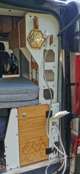 Rear campervan setup featuring an outdoor shower, hexagonal mirror, and modular storage. Perfect for RV rental trips.. Renault Trafic 2023