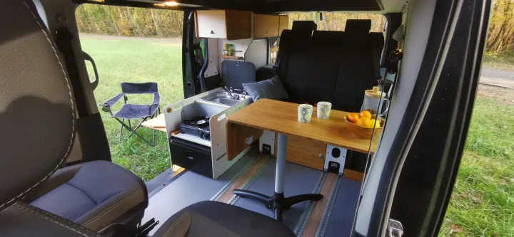 Experience adventure with this rv rental! Modern camper van interior, kitchenette, dining table, and serene outdoor view.. Renault Trafic 2023