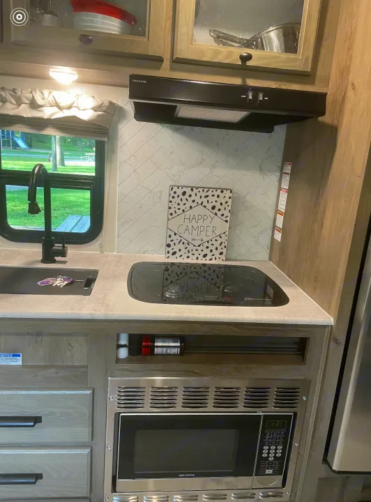 Modern RV rental kitchen featuring a sink, stovetop, microwave, and stylish backsplash. Perfect for your next adventure!. Forest River Surveyor Legend 2023