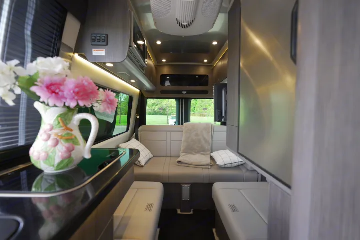 Spacious RV rental interior: modern lounge seating, kitchen counter with flowers, and overhead storage for comfortable travel.. Airstream Interstate 2022
