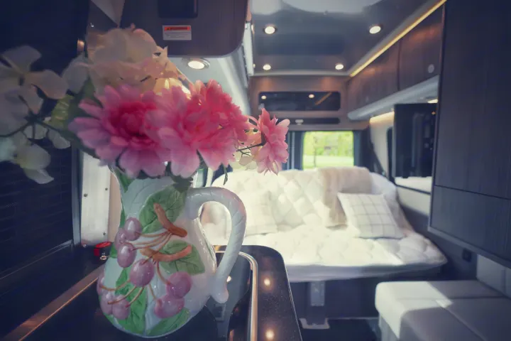 This inviting RV rental interior features a cozy bedroom, kitchenette with flowers, and modern amenities, ready for your next adventure.. Airstream Interstate 2022