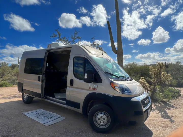 Ram ProMaster rv rental van parked in a sunny desert landscape with a saguaro cactus and open side door, showing interior.. Dodge Promaster- Summit X Edition OA9 2021