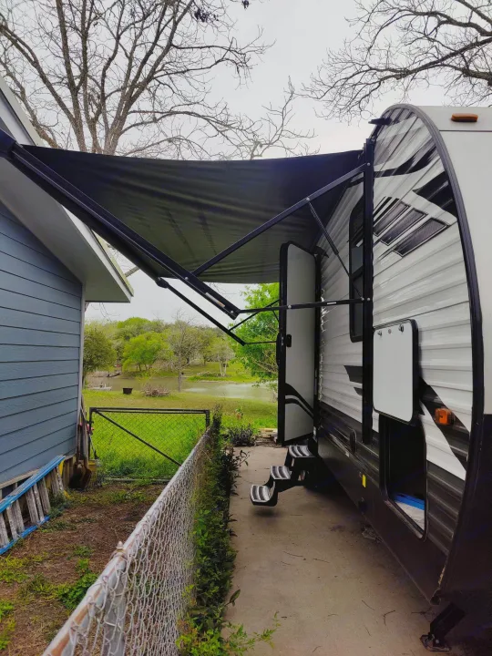 RV rental with awning extended, parked beside a house, offering a serene outdoor experience overlooking a body of water.. Forest River Evo 2022