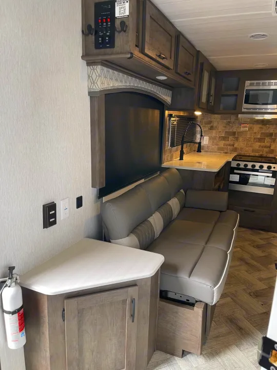 RV rental interior: cozy living space with gray sofa, full kitchen (sink, stove, microwave), overhead cabinets, and herringbone floor.. Forest River Evo 2022