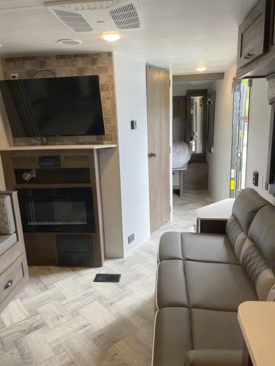 Modern RV rental interior: living room with sofa, TV, electric fireplace, leading to bedroom. Herringbone floor.. Forest River Evo 2022