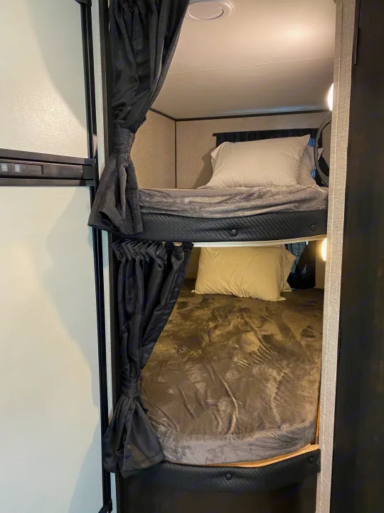 Inside an RV rental: Two neat bunk beds with privacy curtains, bedding, and lights. Great for travelers.. JAYFLIGHT 242BHSW-G 2023