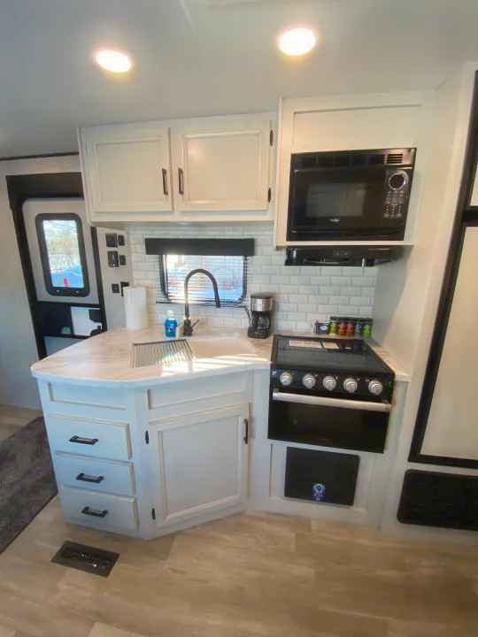 Modern kitchen in this RV rental, featuring white cabinets, subway tile backsplash, and full appliances for comfortable travel.. JAYFLIGHT 242BHSW-G 2023