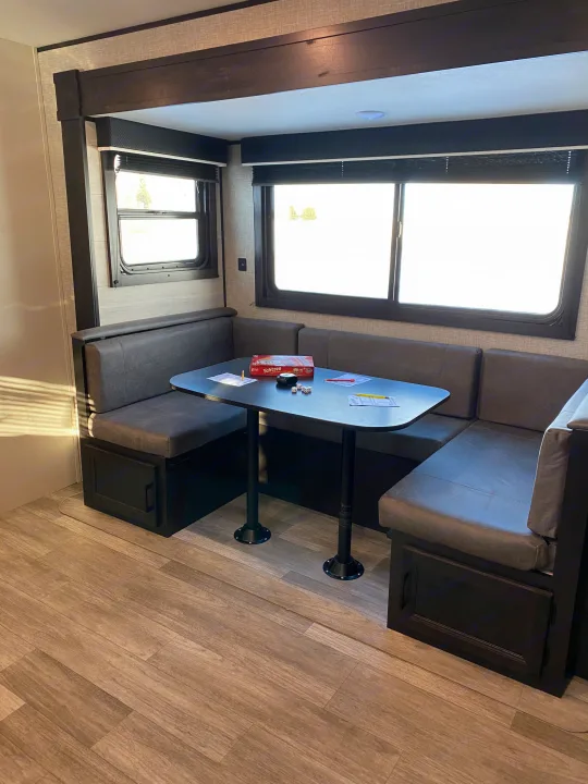 Cozy RV rental dinette with a dark table, grey booth seating, and large windows. Yahtzee set ready for fun.. JAYFLIGHT 242BHSW-G 2023