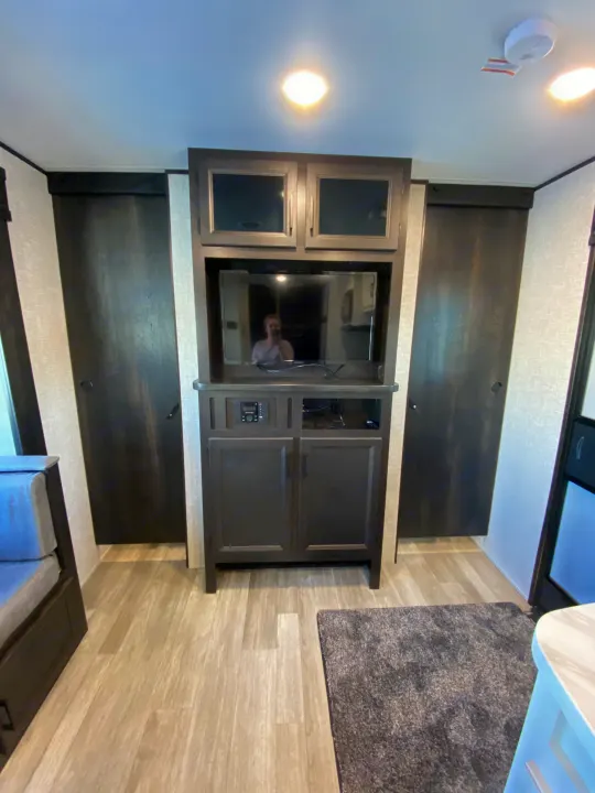 RV rental interior: modern entertainment center with TV, dark cabinets, flanking closets, and light wood-look floor.. JAYFLIGHT 242BHSW-G 2023