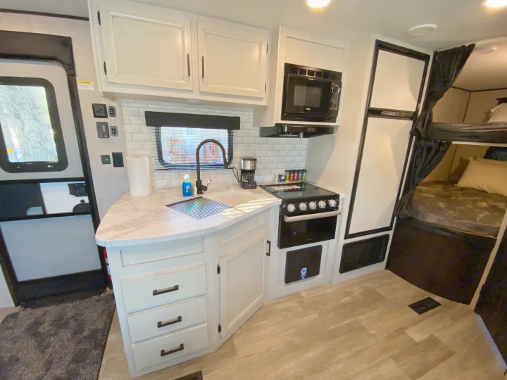 Clean RV rental interior featuring a full kitchen with light counters, black appliances, and a cozy bunk bed area.. JAYFLIGHT 242BHSW-G 2023