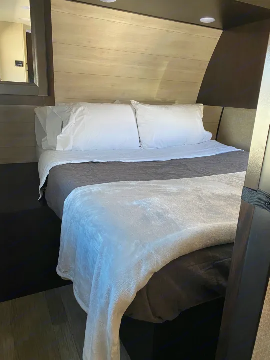 This cozy RV rental sleeping area features a neatly made bed with white linens & a plush blanket, set against wood-paneled walls.. JAYFLIGHT 242BHSW-G 2023