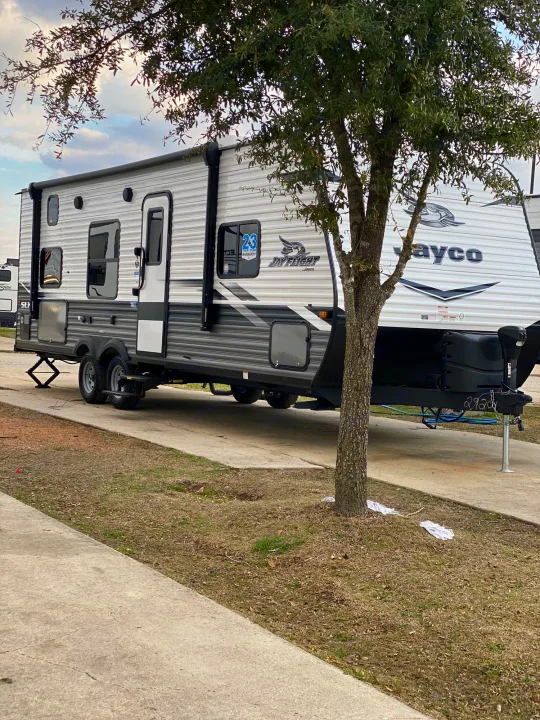 A white and grey Jayco RV rental travel trailer is parked on a concrete pad at a campsite, with a tree in front.. Jayco Jay Flight Bungalow 2022