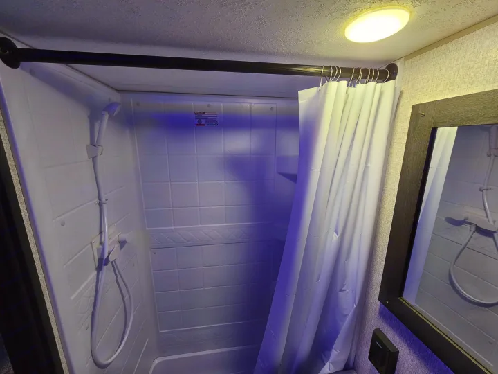 Compact RV rental shower stall featuring a white curtain, handheld showerhead, and wall-mounted mirror. Ideal for road trips.. KZ 312 Bunk House 2022