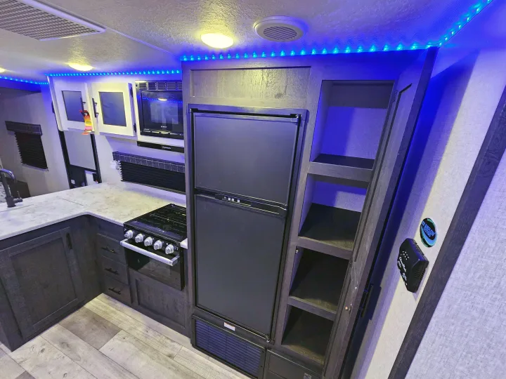 Modern RV rental kitchen features blue accent lighting, a fridge, stove, microwave, and ample storage.. KZ 312 Bunk House 2022
