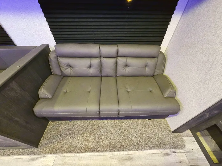 Compact gray sofa with white stitching in a modern RV rental interior, featuring pleated blinds and soft carpet.. KZ 312 Bunk House 2022