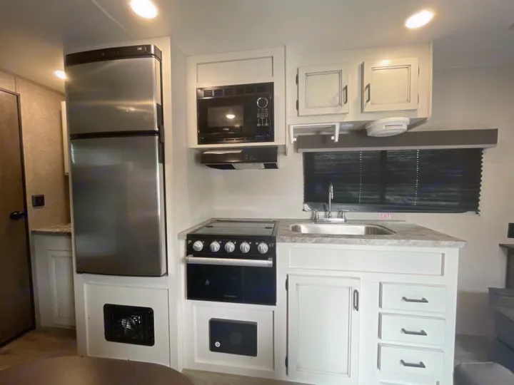 RV rental kitchen with stainless steel fridge, microwave, and range. White cabinets, sink, and window create a functional, modern space.. Highland Ridge RV Open Range 2021