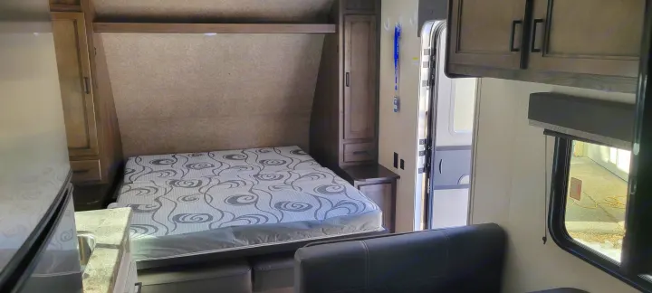 Inside an RV rental: a compact interior with a fold-down bed, kitchen area, storage cabinets, and open main door, ideal for travel.. Highland Ridge RV Open Range 2021