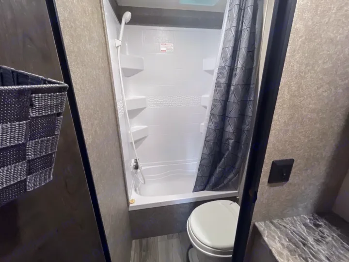 Step inside this RV rental bathroom featuring a shower with curtain, toilet, and small counter area.. Highland Ridge RV Open Range 2021