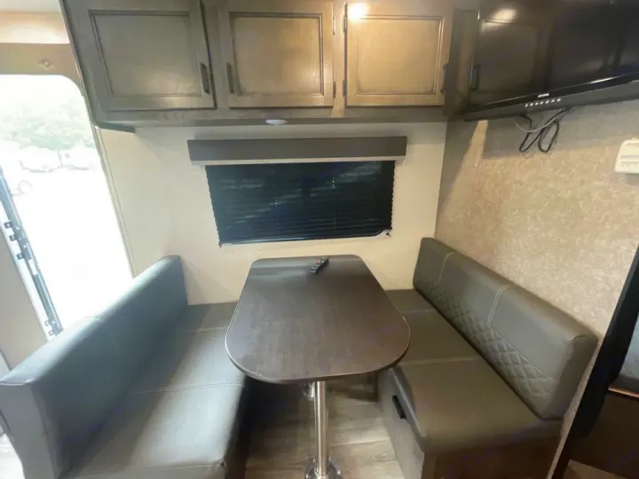 This RV rental features a cozy dinette with a central table, cushioned benches, overhead cabinets, and a wall-mounted TV.. Highland Ridge RV Open Range 2021