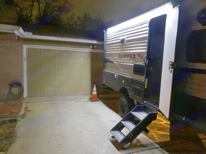 Night view of an RV rental travel trailer with steps and bright LED lights, parked in a driveway next to a garage.. Forest River Coachmen RV Clipper Ultra-Lite 17BH 2022