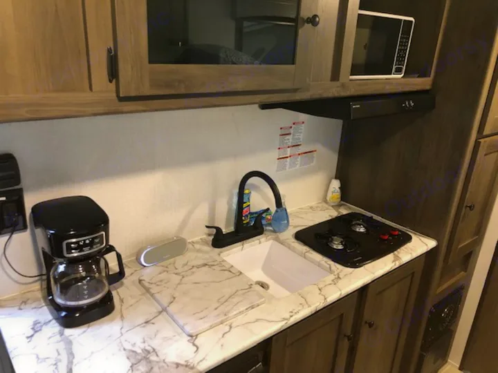 This RV rental kitchen features a black coffee maker, white sink, cooktop, and built-in microwave.. Forest River Coachmen RV Clipper Ultra-Lite 17BH 2022