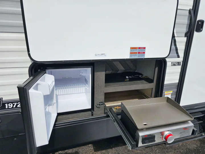 RV rental's outdoor kitchen, showing an open mini-fridge and pull-out griddle for convenient cooking.. KZ 312 Bunk House 2022