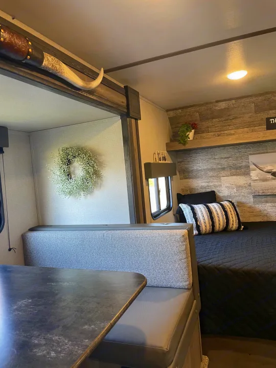 Cozy RV rental interior: dinette with longhorn decor and a bed area with rustic wood accents.. Keystone Springdale 2021