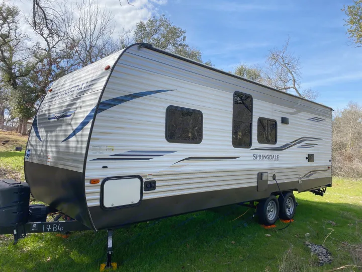 Modern Springdale travel trailer, ideal for RV rental, resting on green grass under a clear sky.. Keystone RV Springdale 2021