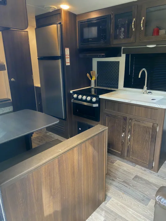 Well-equipped RV rental kitchen and dinette area, featuring a refrigerator, microwave, stove, sink, and comfortable seating.. Keystone RV Springdale 2021