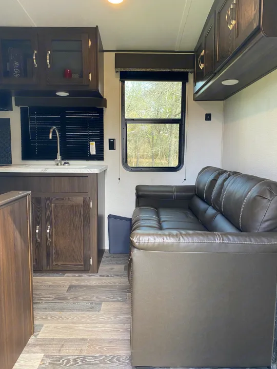 This RV rental interior features a modern kitchen, comfortable leather sofa, and large windows overlooking nature.. Keystone RV Springdale 2021