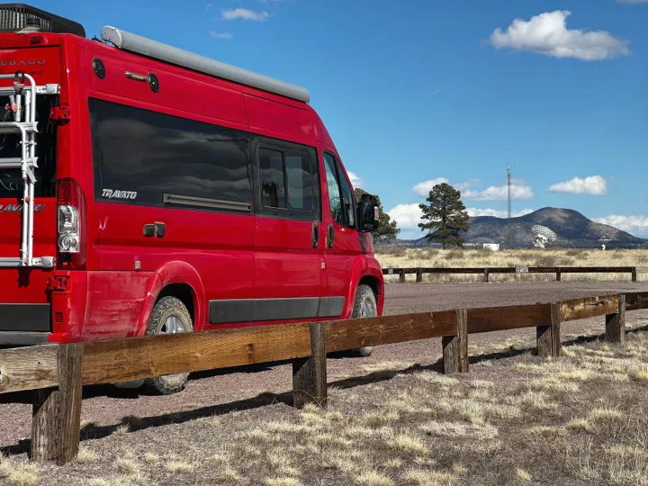 Red Winnebago Travato RV rental parked. Features a scenic backdrop with distant radio telescopes & mountains.. Winnebago Travato 2015