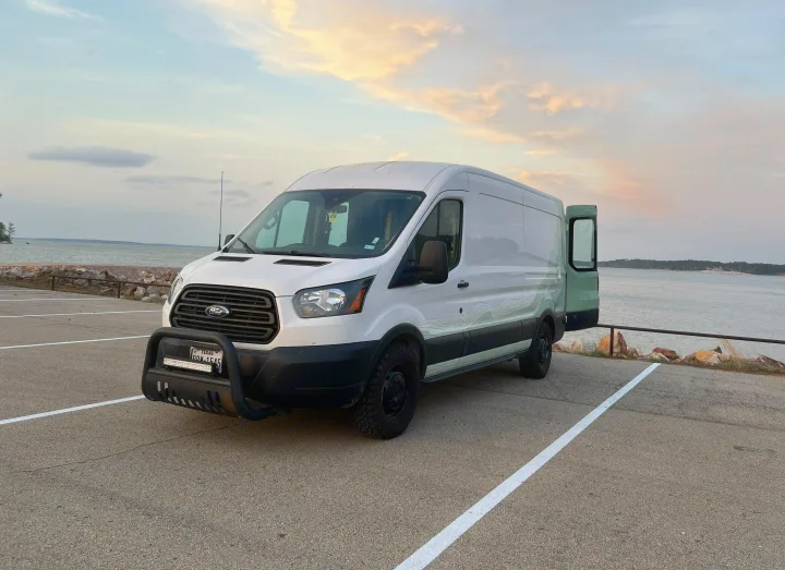 An RV rental ready for adventure: white Ford Transit camper van parked lakeside at dusk with the back door open, perfect for van life.. Ford Transit 2019
