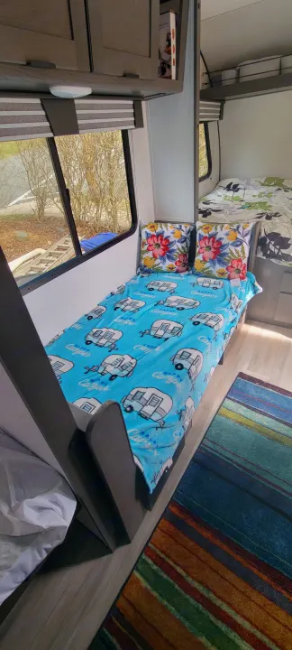 Inside a modern RV rental, find a vibrant bunk bed with a camper-themed blanket & floral pillows, creating a cozy sleeping space.. Heartland RVs Mallard 2022