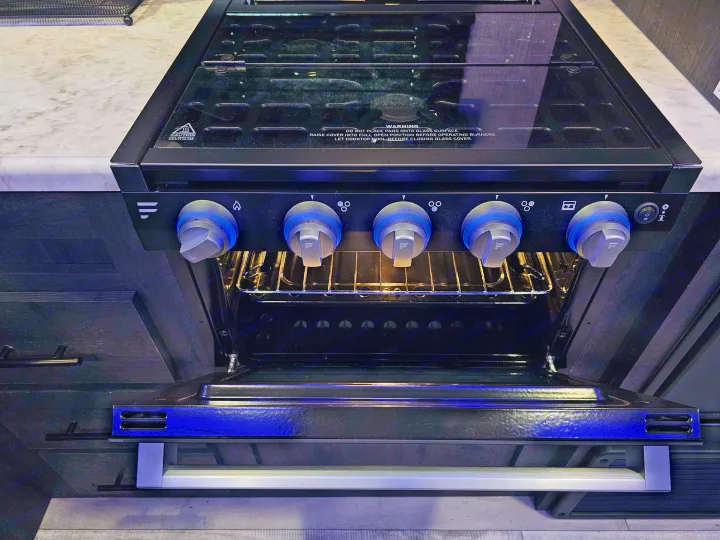 RV rental kitchen: a modern stove/oven with illuminated blue control knobs and a glass cooktop cover. Oven door open.. KZ 312 Bunk House 2022
