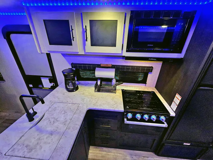 Modern RV rental kitchen with blue LED accent lighting, featuring a sink, stove, microwave, and coffee maker.. KZ 312 Bunk House 2022