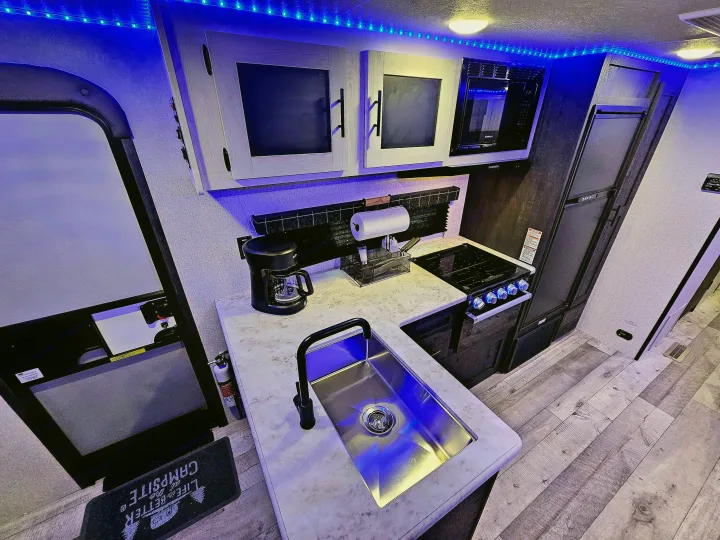 Modern RV rental kitchen showing sink, stove, microwave, fridge, and blue lights. Perfect for a comfortable campsite stay.. KZ 312 Bunk House 2022
