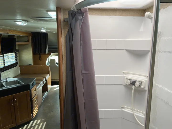 Inside an RV rental: a modern white shower stall and a well-equipped kitchen with a double sink and dinette.. Winnebago Minnie Winnie 2018