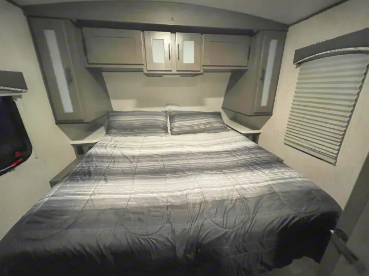 Comfortable RV rental bedroom featuring striped bedding, built-in storage, and window blinds, perfect for travel.. Cruiser RV MPG Ultra Lite 2021