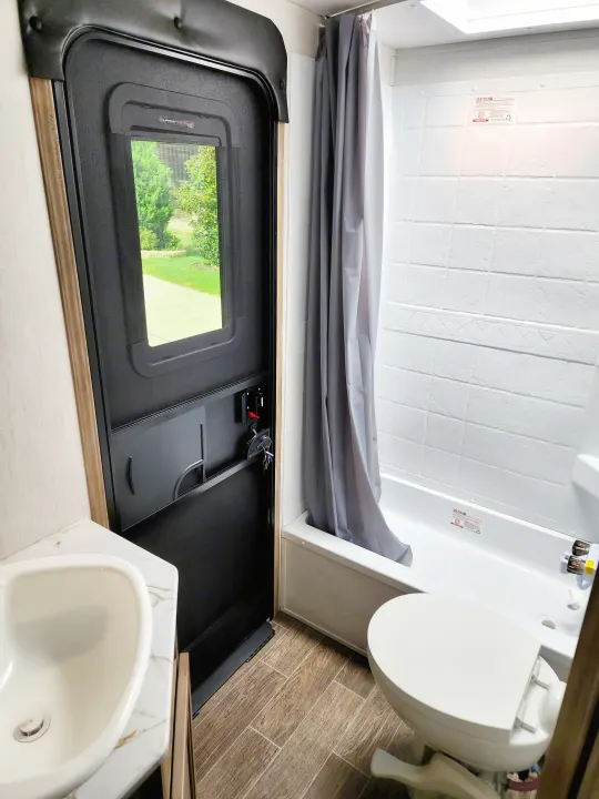 Compact RV rental bathroom features a sink, toilet, and shower/tub combo. The screen door offers a view outside while camping.. Forest River Cherokee Alpha Wolf 2022